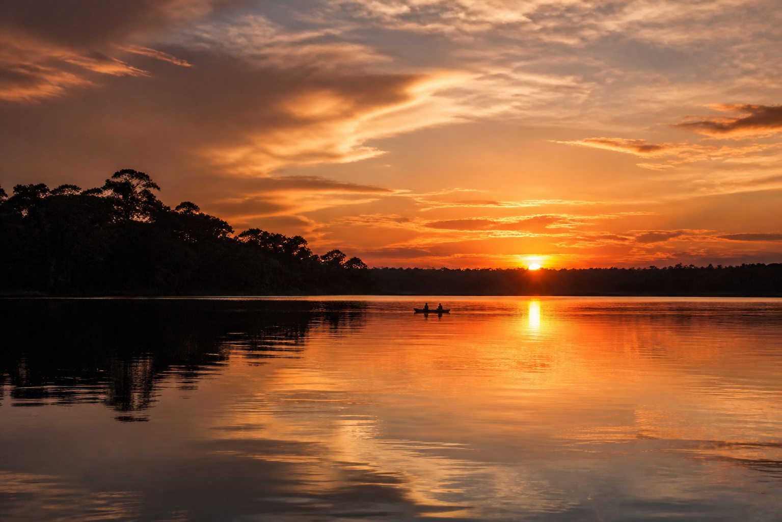 Golden Amazon sunset over calm water and forest silhouettes.
